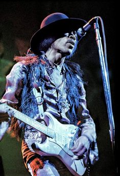 a man with a hat and feather vest playing a guitar in front of a microphone