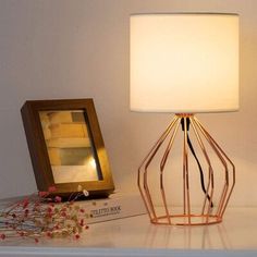 a lamp sitting on top of a white table next to a book and framed photograph