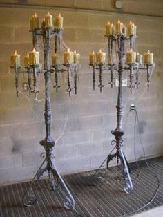 two metal candelabras with candles on them in front of a brick wall