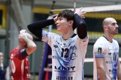 three men are playing volleyball on a court while one man holds his hands up in the air