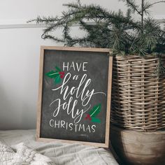 a christmas sign sitting on top of a bed next to a basket filled with pine cones