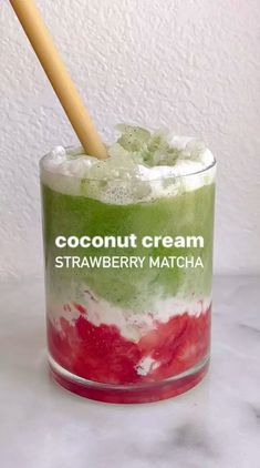 a glass filled with ice cream and strawberries on top of a white counter next to a wooden spoon