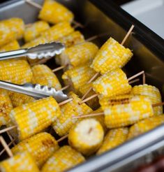 corn on the cob with tongs and toothpicks in a metal container