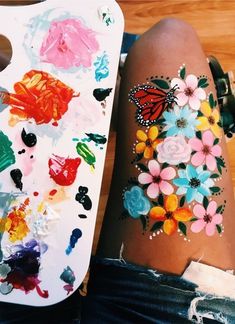 a woman's arm with flowers and butterflies painted on it, next to a painting board