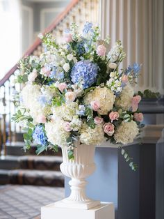 a vase filled with white and blue flowers on top of a table next to a stair case