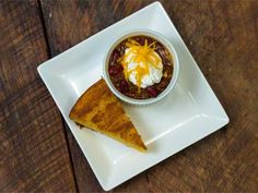 a white plate topped with a piece of pie and a bowl of chili cheese soup