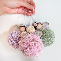 a hand is holding an ornament with small dolls hanging from it's sides