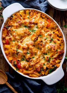 a white casserole dish filled with pasta and vegetables on top of a wooden table