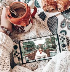 a person holding a cell phone on top of a blanket next to a cup of coffee