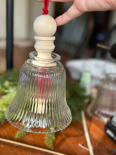 a person is holding a small glass bell with a red top and wooden dows