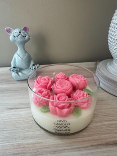 a glass bowl filled with pink roses on top of a table next to a cat figurine