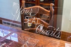 a wooden chair sitting in front of a window with the words your seat awaits written on it