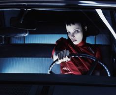 a woman driving a car in the dark with her hand on the steering wheel and looking at the camera