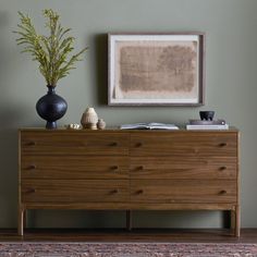 a wooden dresser with two vases on top of it next to a framed painting