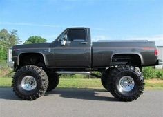 a large black truck parked on top of a parking lot next to a grass covered field