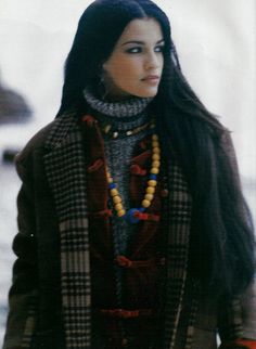 a woman with long black hair wearing a plaid jacket and scarf, standing in the snow