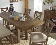 a dining room table with chairs and a vase on it's end, in front of a window