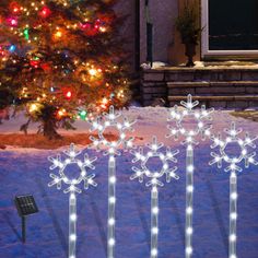 lighted snowflakes in front of a christmas tree on a snowy yard with lights