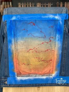 the back of a pair of jean pants with an image of clouds painted on it