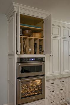 an oven built into the wall in a kitchen with white cupboards and counter tops