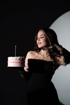 a woman in a black dress holding a cake with a lit candle on top of it