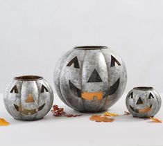 three pumpkin shaped vases sitting next to each other on a white surface with leaves scattered around them