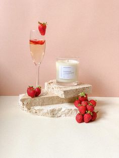 a candle and strawberries on a table next to a glass of wine in front of a pink wall