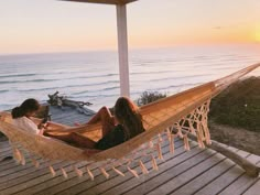 two women sitting in a hammock looking at the sunset over the ocean,