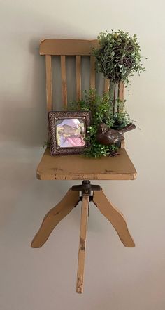 a small wooden chair with a potted plant on it's back and an old photo frame sitting on top of it