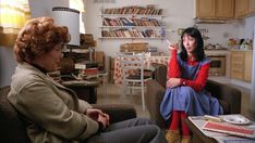 two women sitting on couches in a living room with bookshelves behind them