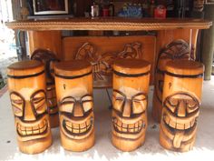 three wooden tiki style stools with faces painted on the sides and one sitting next to them