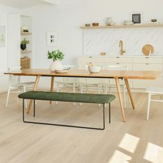 a dining room table and bench in front of a white kitchen with wood flooring