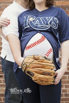 a pregnant woman wearing a catchers mitt poses for a photo with her husband