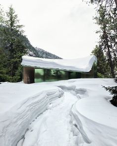 a snow covered path leading to a building in the middle of some trees and mountains