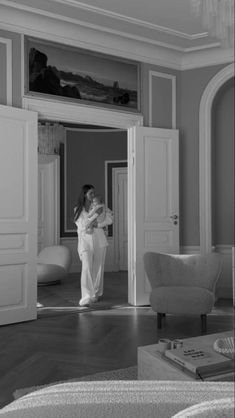 black and white photograph of a woman standing in a living room with doors open to another room