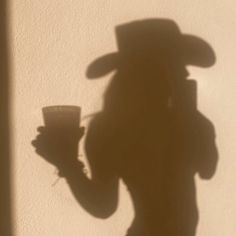 the shadow of a man in a hat holding a cup