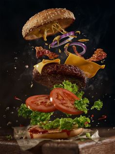 a hamburger falling into the air with lettuce, tomato and onion on it