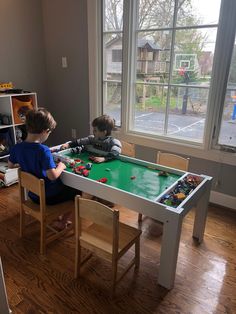 two young boys play with toys at a table in front of a large open window