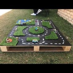 a table made out of wood and grass with toy cars on the road in the middle