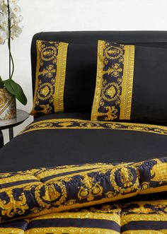 a bed with black and gold comforters on top of it next to a flower vase