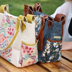 three floral bags sitting on top of a wooden table next to a woman's handbag