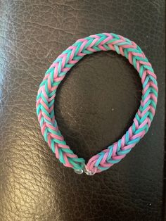 a pink and blue braided bracelet sitting on top of a black leather table next to a cell phone