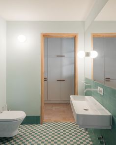 a bathroom with green and white checkered flooring next to a toilet, sink and mirror