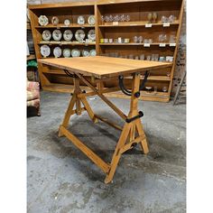 a wooden table sitting on top of a floor next to shelves filled with glassware