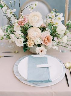 a table setting with white and pink flowers in a vase on top of a plate