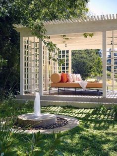 a white pergoline covered patio with an orange couch and pillows on the bench