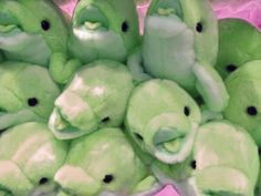 a group of green stuffed animals sitting next to each other on a pink surface with black eyes