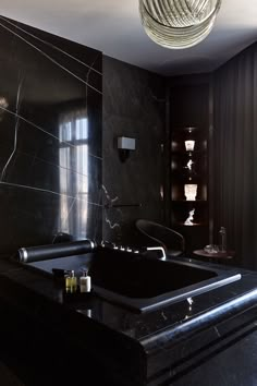 a bathroom with black marble walls and floor, along with a large bathtub in the center