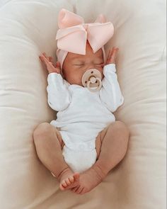 a baby with a pacifier in its mouth laying on a white pillow wearing a pink bow