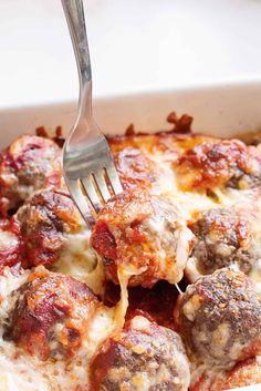 a fork is stuck into some meatballs in a casserole dish with cheese and sauce